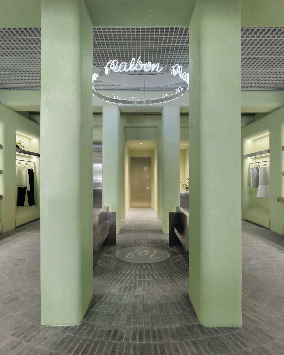 The centre of Malbon Golf Miami designed by 22RE, featuring four stuccoed pastel green columns. An aluminum ring hangs in the middle with the store's name written out in cursive neon.