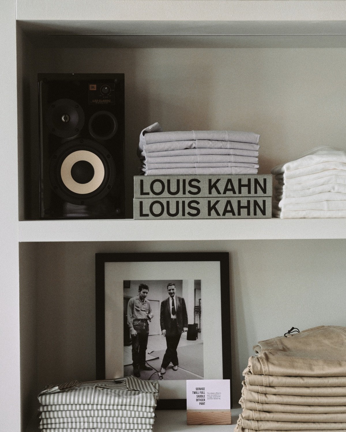 A black speaker sits next to a stack of Louis Kahn books and light khaki trousers.