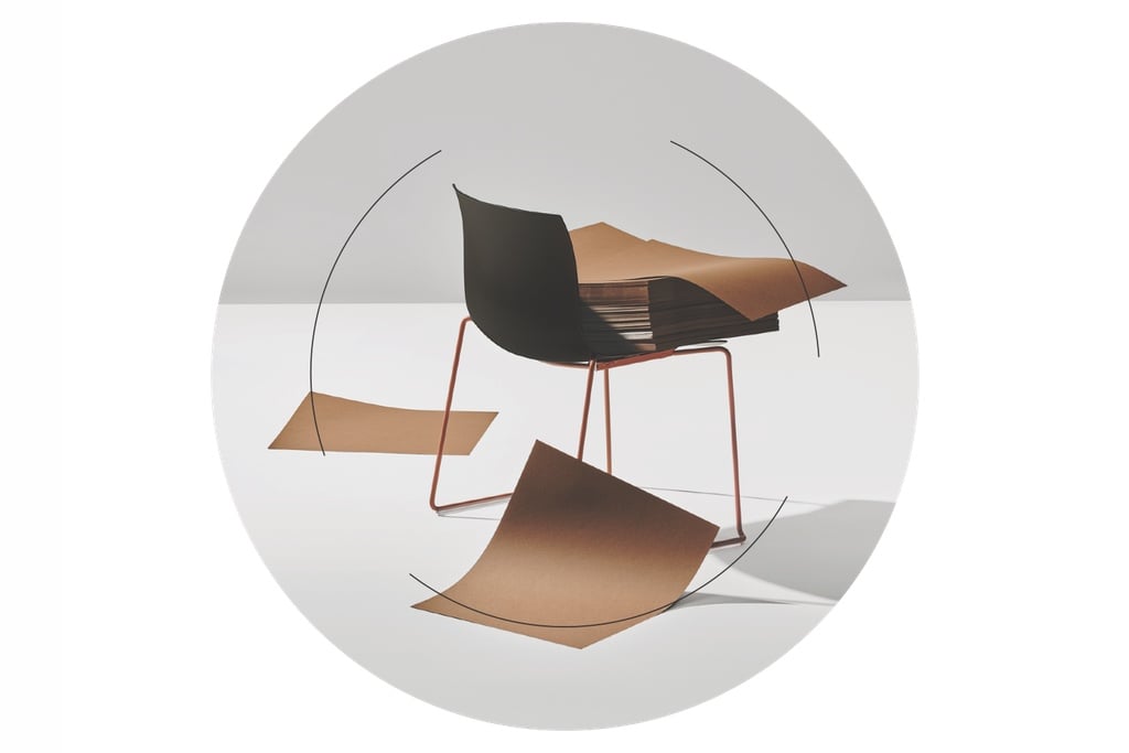 Arper's recycled paper Catifa Carta chair with a stack of brown paper sheets resting on it. On top of the image, thin black lines form a circle, highlighting an example of circular design in the furniture industry.