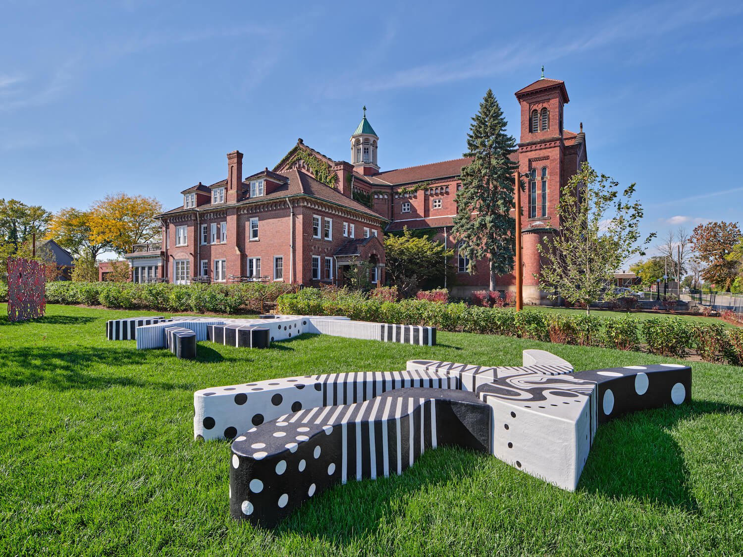 A worm's eye view of the Charles McGee sculpture park at Little Village Detroit, with The Shepherd and the rectory house visible in the background.