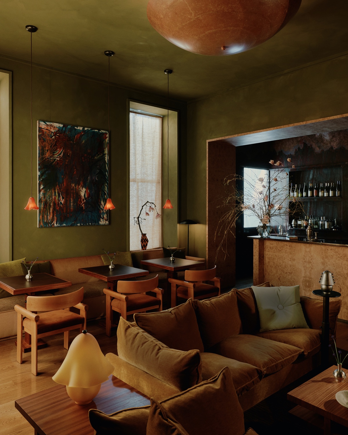 The bar room at Quarters in New York featuring a velvet sofa and three cocktail tables with wooden tables and glowing orange glass pendants hanging above. The room is painted moss green, and to the right is a burled wood bar table.