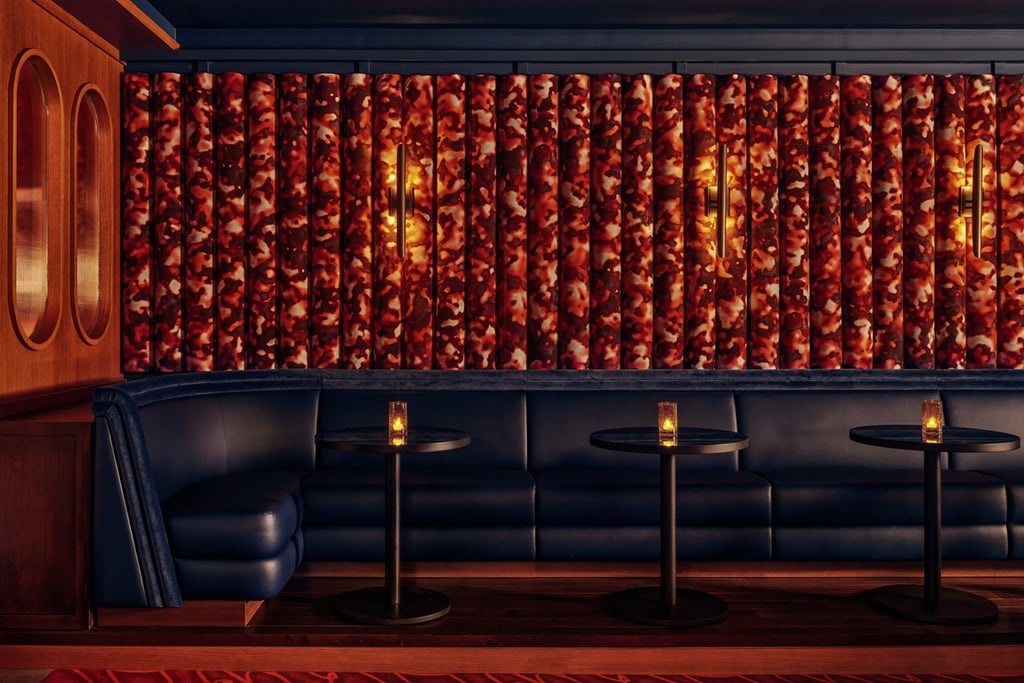 A view of the blue banquette seating at New York piano bar So&So's. Red camo print fabric lines the wall.