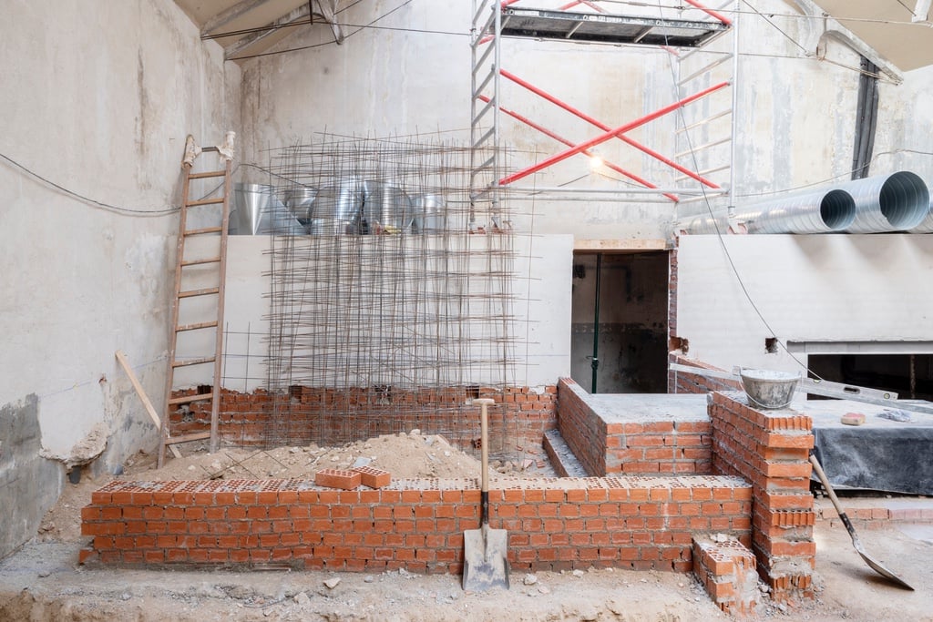 A view of an industrial building under renovation, featuring in-progress brickwork and steel pipes.