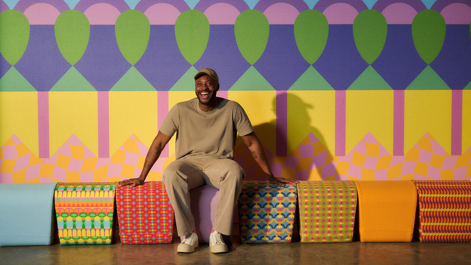 Yinka Ilori sits in front of a wall clad in his collection with Momentum