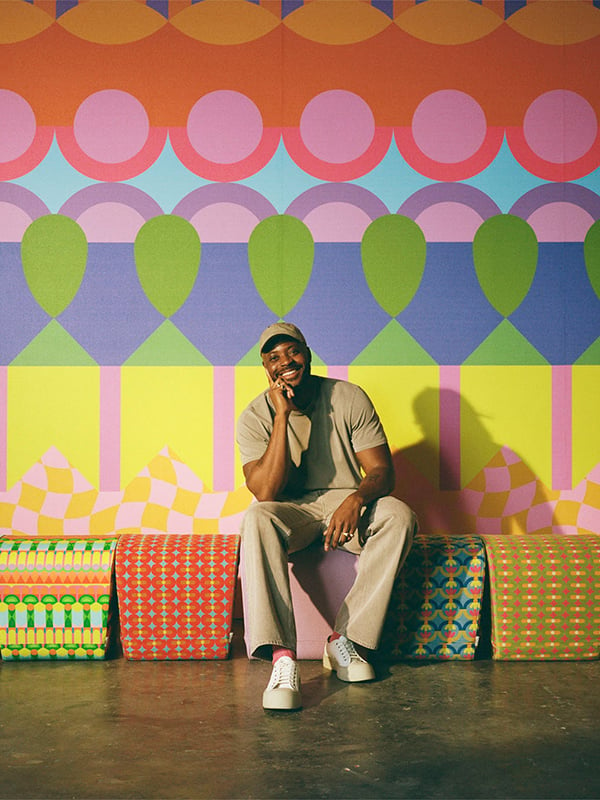 Yinka Ilori sits in front of a wall clad in his collection with Momentum