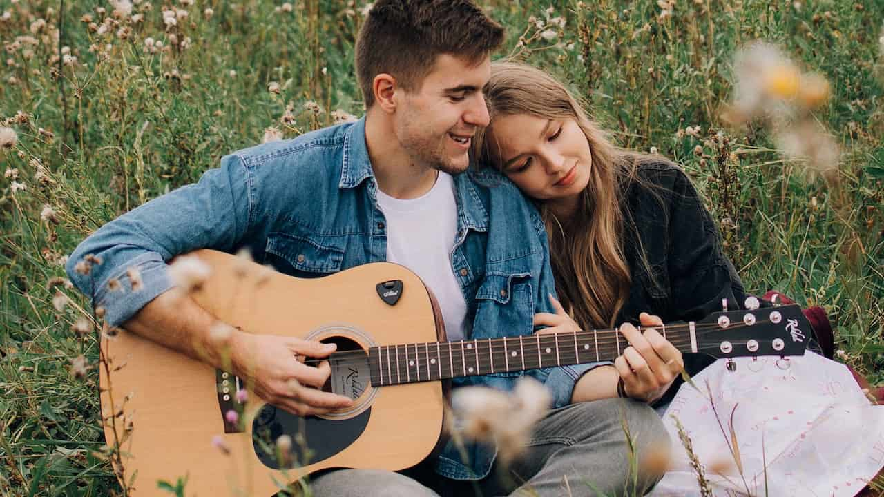 Man playing guitar while woman leans on his shoulder